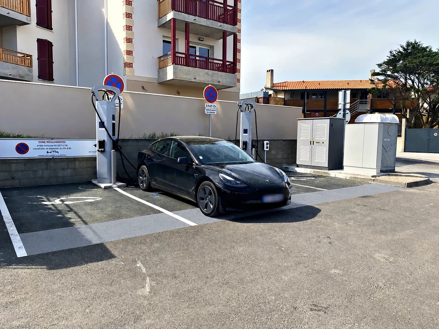 Voiture électrique noire en charge devant deux bornes, au pied d’un immeuble.